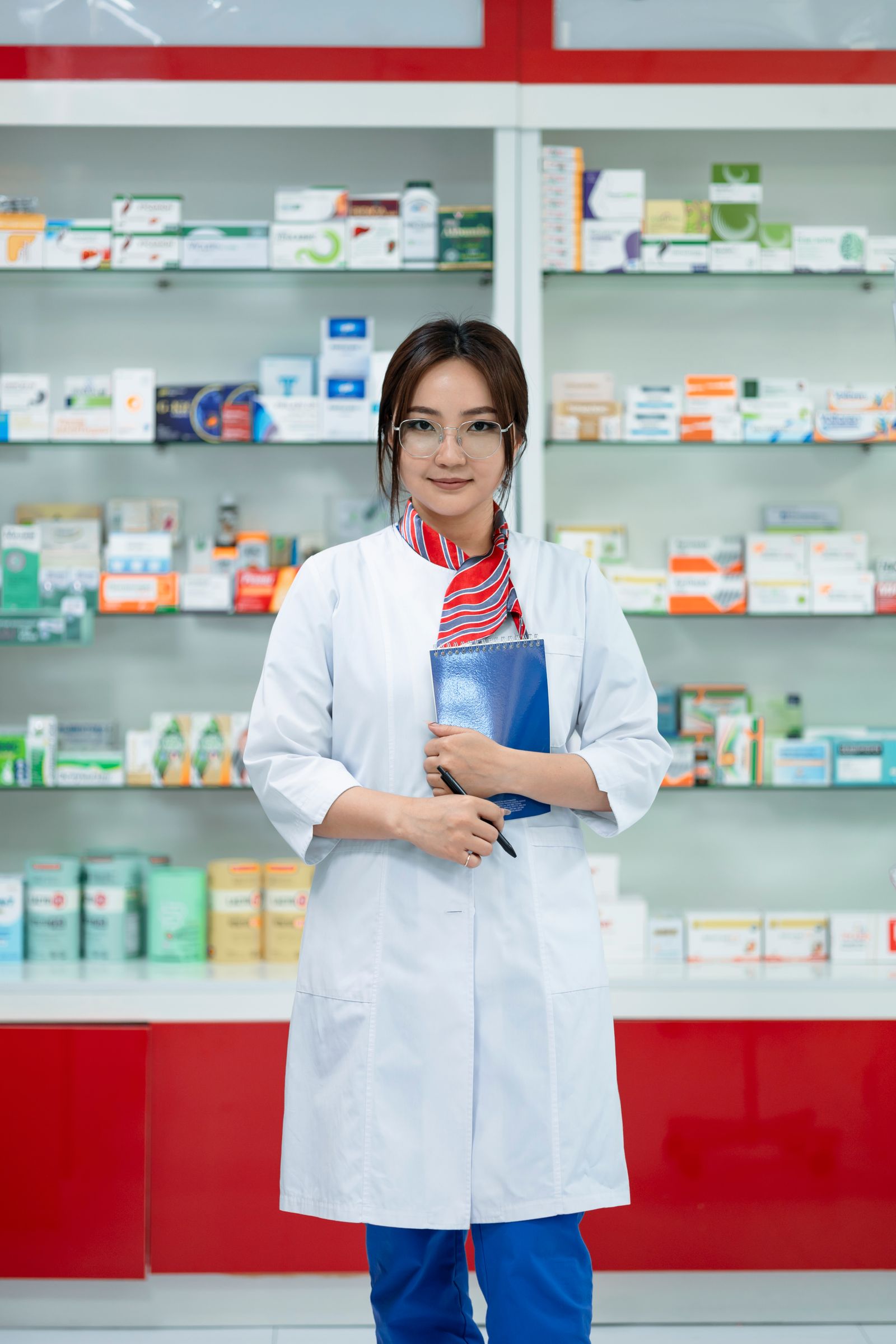 A pharmacy professional holding a notebook in a pharmacy